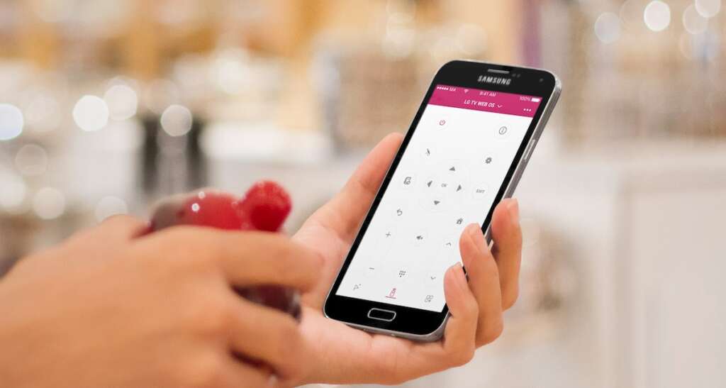A hand holding an Android smartphone with LG tV remote app on the screen